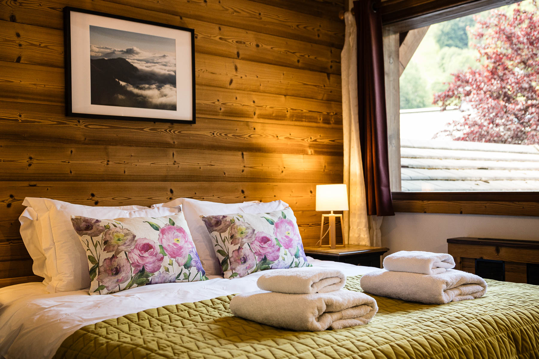 Double bed with floral cushions, green bedding and fresh towels at Chalet Coffy in Morzine