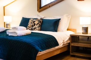 Double bed with deep blue bedding, fresh towels and bedside lamps at Chalet Coffy