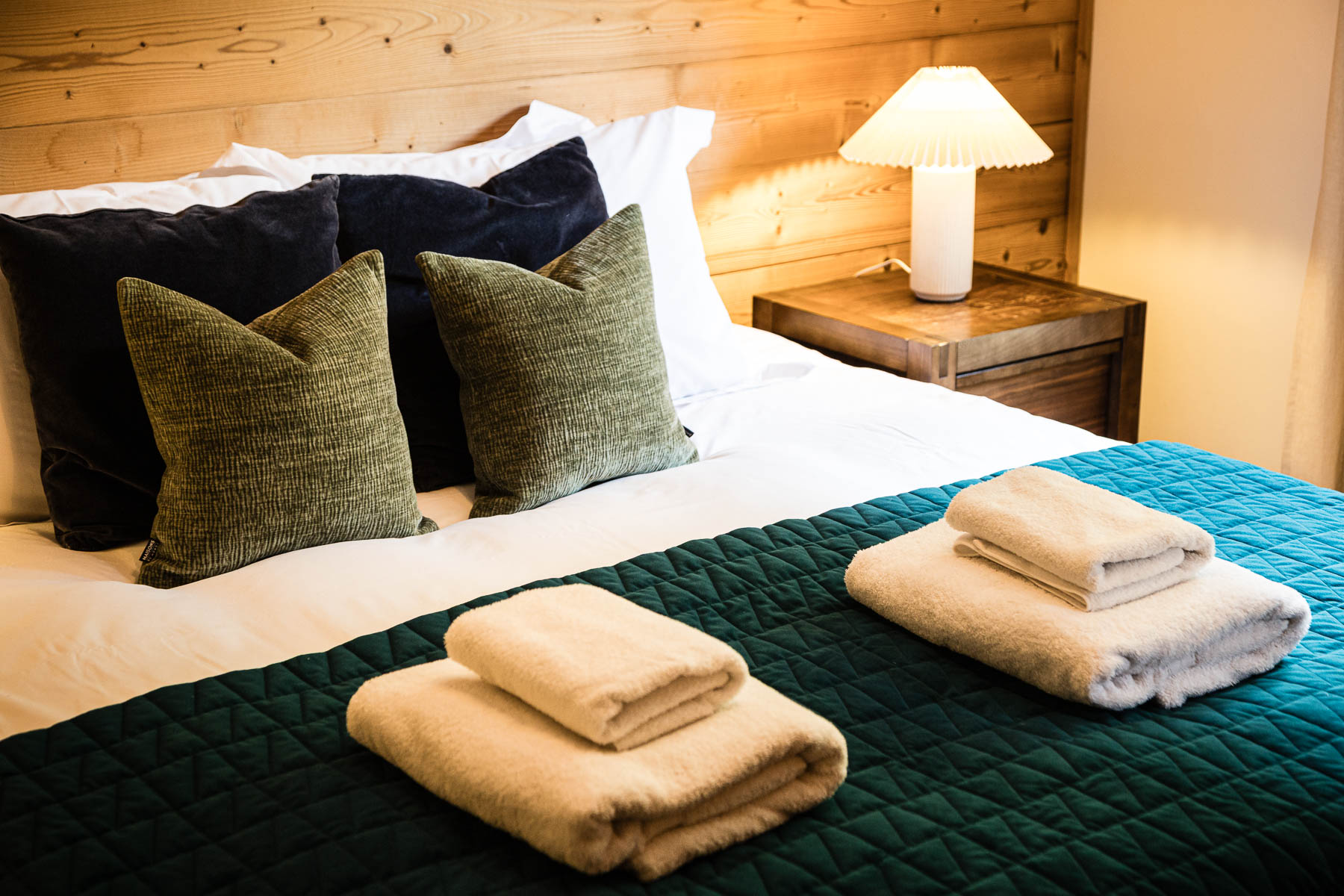 Close-up of a double bed with green and blue cushions, quilted bedding and fresh towels