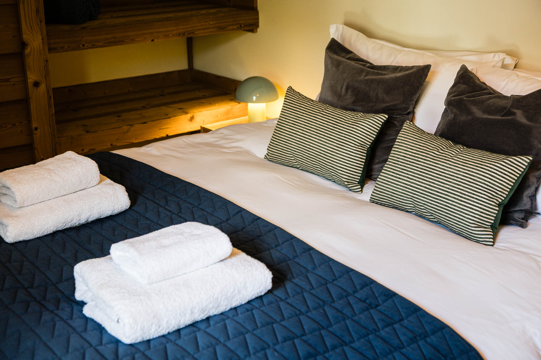 Double bedroom with blue quilted bedding, striped cushions and fresh towels at Chalet Coffy