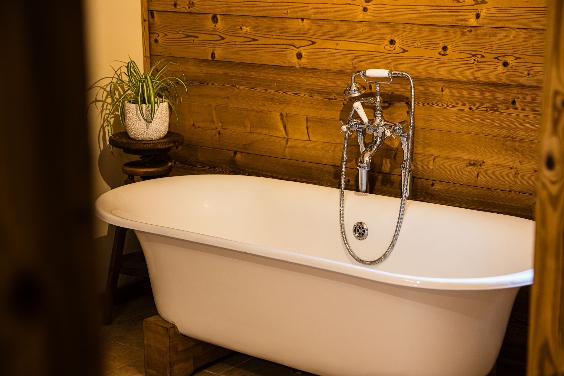 Freestanding roll-top bath with traditional chrome taps and timber wall at Chalet Coffy