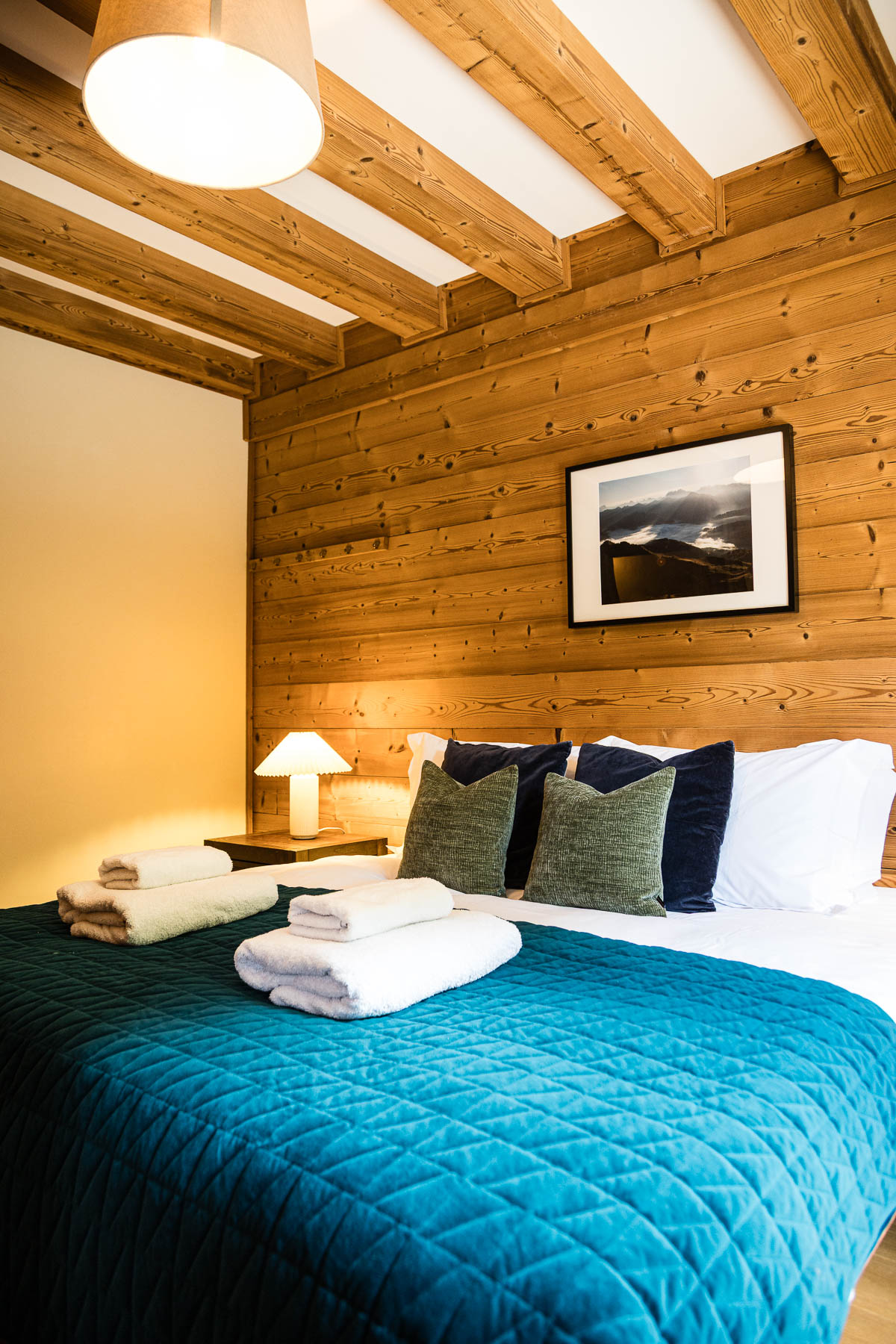 Warm alpine double bedroom at Chalet Coffy with exposed timber beams and blue-green bedding